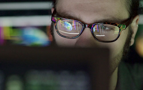 person with glasses behind a computer screen